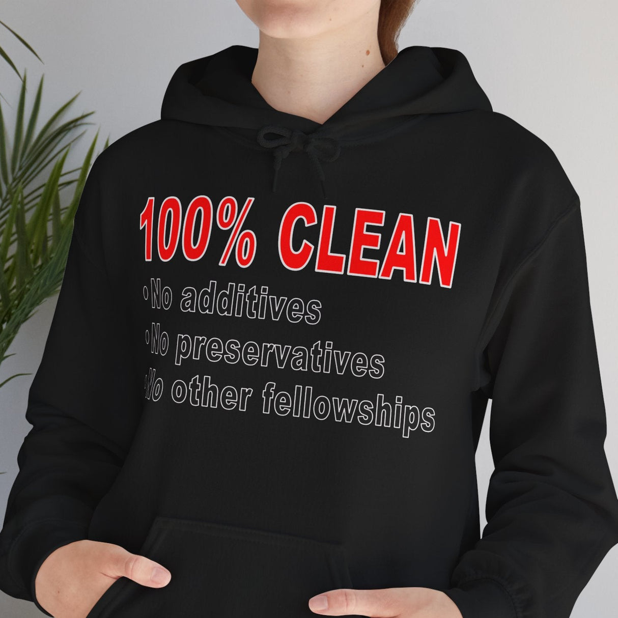 Person wearing a black hoodie with red and white text in a room with a plant.