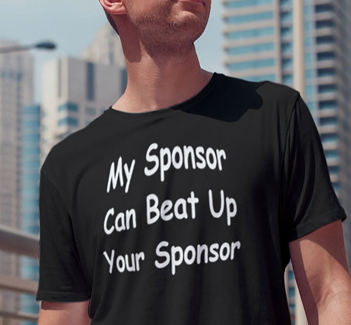 A man wearing sunglasses is standing on a bridge wearing a black T-shirt with the text 'My Sponsor Can Beat Up Your Sponsor' on the front.