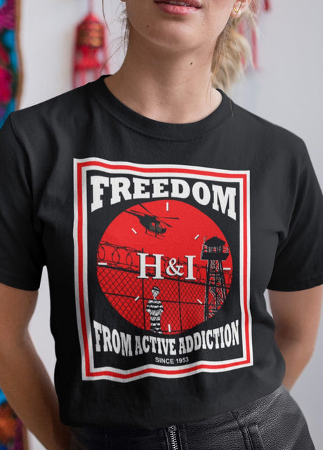 Person wearing a black t-shirt with a graphic design and text, standing against a colorful wall.